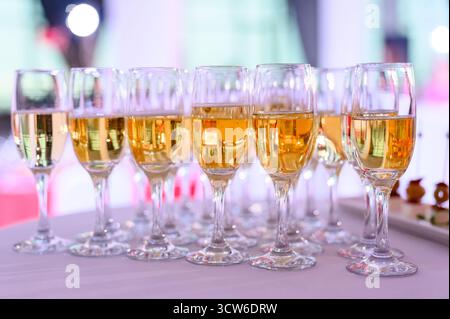 Eine Reihe von Gläsern gelben Sekts oder Sekt auf einem Buffettisch. Nahaufnahme von Sektgläsern mit goldenem Getränk auf weißer Tischdecke Stockfoto