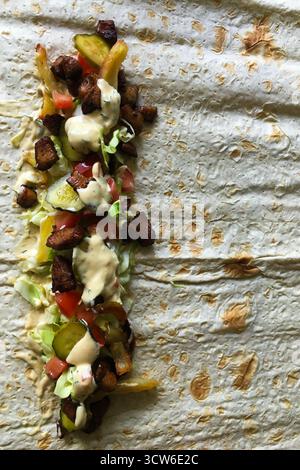 Traditionelle Shawarma-Wrap mit gegrilltem Fleisch, frischem Gemüse und Sauce, präsentiert in warmem natürlichem Licht Stockfoto
