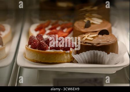 Nahaufnahme von Himbeertörtchen und Schokoladenkuchen. Süße Desserts mit Beeren und Mandeln auf einem Teller in einer Konditorei Stockfoto
