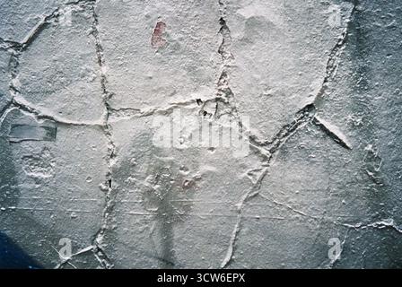 Nahaufnahme einer weißen Wand mit tiefer, gerissener Fassade. Raue Textur zeigt Zeit und Zerfall. Aufgenommen auf analogem Film mit natürlichem Licht. Stockfoto