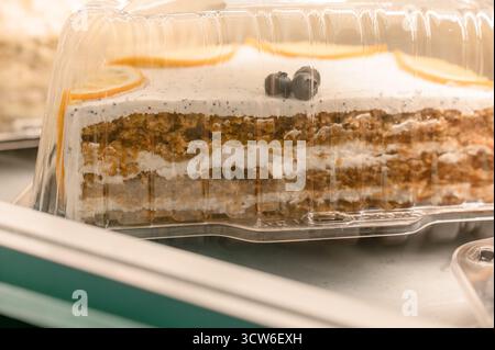 Nahaufnahme von Karottenkuchen oder Biskuitkuchen mit Sahne. Ein Stück Kuchen mit Mohn und Zitrusfrüchten in einem Einwegbehälter zum Verkauf Stockfoto
