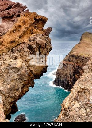 Dramatischer Madeira Cliff Arch View - intensiver vertikaler Schuss einer zerklüfteten vulkanischen Felsformation, die einen natürlichen Bogen mit Blick auf das türkisfarbene Atlanti bildet Stockfoto
