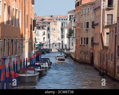 Schmaler venezianischer Kanal mit Turm und Polizeiboot - Blick auf einen schmalen venezianischen Kanal, der von farbenfrohen Gebäuden gesäumt ist, mit einer entfernten weißen Glocke Stockfoto