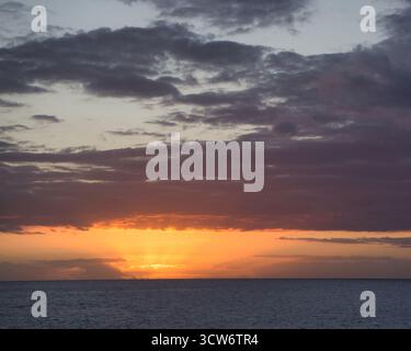 Lebendiger Sonnenuntergang über dem Atlantischen Ozean - dramatischer Sonnenuntergang im Ozean mit intensivem Orange und gelbem Leuchten unter einem Himmel voller violetter und grauer Sturmwolken. Stockfoto
