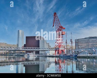 Bilbao Stadtbild mit Carola Crane - Blick auf die Bilbao Uferpromenade mit dem roten Carola-Kran und moderner Architektur, die sich im Nervion River, B, widerspiegelt Stockfoto