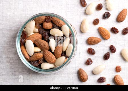 Mandeln mit Samenmantel und blanchiert, mit Rosinen gemischt, in Glasschale, auf Leinen. Trail Mix, bekannt seit dem 17. Jahrhundert. Stockfoto