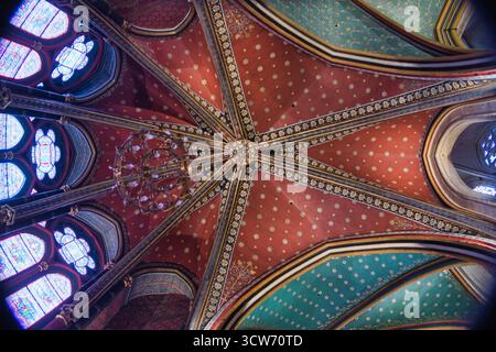 Gotische Gewölbe und Wandgemälde von Sainte-Chapelle – aus dem niedrigen Winkel sehen Sie reich bemalte gotische Rippengewölbe in Rot, Gold und Petrol sowie ein großes Kruzifixi Stockfoto