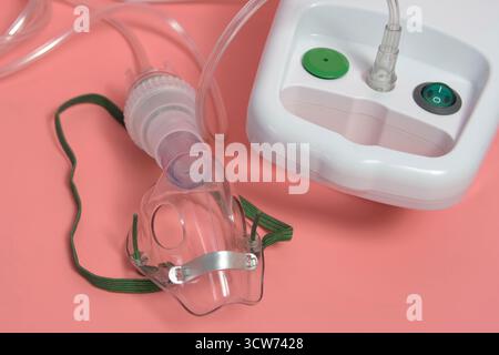 Eine durchsichtige medizinische Kunststoffmaske mit grünem Band ist an einem Schlauch an einem Inhalationsgerät befestigt Stockfoto