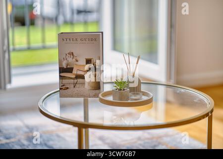 Stilvolle Inneneinrichtung mit einem Dekorationsbuch und modernen Accessoires auf einem Glastisch in hellem Wohnbereich Stockfoto