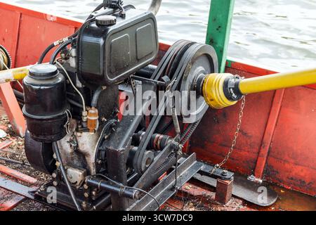 Nahaufnahme einer schwarzen Marine-Windenanlage auf einem roten Bootsrumpf mit schwarzem Motor, Riemen und einer hellgelben Antriebswelle. Ideal für nautische Ma Stockfoto