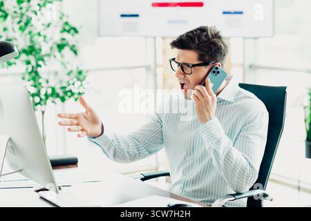 Konzentrierter Geschäftsmann in einer professionellen Büroumgebung, der während der Arbeit am Computer telefoniert Stockfoto