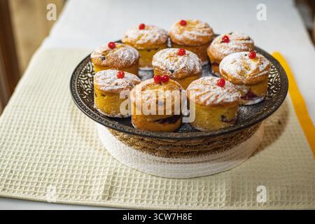 Frisch gebackene hausgemachte Muffins mit Puderzucker bestreut und mit roten Beeren auf einem Metallteller dekoriert, köstliches süßes Dessert zum Frühstück oder Stockfoto