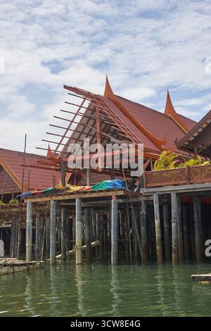 PHUKET, THAILAND - 12. NOVEMBER 2017: Traditionelles thailändisches Pfahlhaus auf dem Wasser mit verzierten roten Dächern und blauem Himmel im Hintergrund. Stockfoto