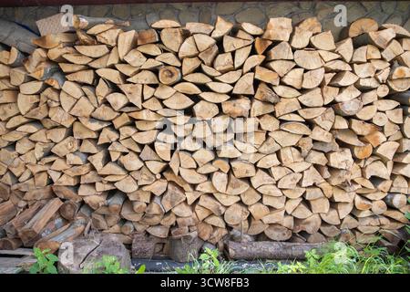 Stapel gehackter Brennholzstämme, die im Freien an einer Steinmauer angeordnet sind. Konzept der erneuerbaren Energien, des ländlichen Lebens und der natürlichen Ressourcen. Stockfoto
