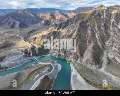 Dramatischer Blick aus der Luft auf den türkisfarbenen Fluss Katun und eine gewundene Straße durch die bergige Landschaft der Republik Altai Stockfoto