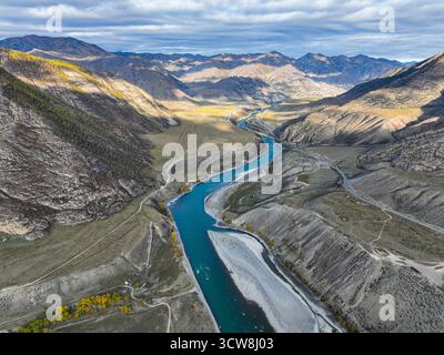 Panoramablick auf den Fluss Katun, der durch ein tiefes Tal fließt und vom Sonnenlicht beleuchtet wird, der Schatten auf die großen, zerklüfteten Berge wirft Stockfoto