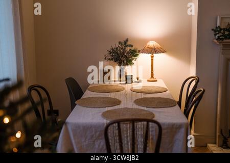 Warm beleuchteter festlicher Esstisch mit rustikaler Einrichtung, Weihnachtsdekoration, Kerzen und gemütlicher Winteratmosphäre. Stockfoto