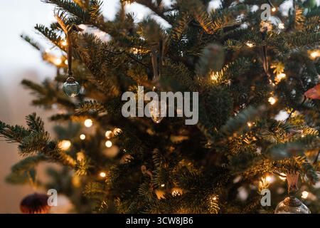 Nahaufnahme eines ästhetischen, minimalistischen Weihnachtsbaums mit Kugeln und warmen Feenlichtern, festlichem Geist, gemütlichen Winterferien. Warme Töne und Gemütlichkeit Stockfoto