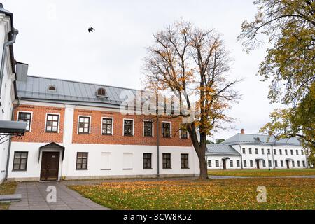 Der Innenhof eines Klosters im Herbst, mit einem historischen Gebäude mit Ziegelsteinmauern und weißen Wänden, einem Pfad und einem Rasen, der mit gelb gefallenen Blättern bedeckt ist Stockfoto