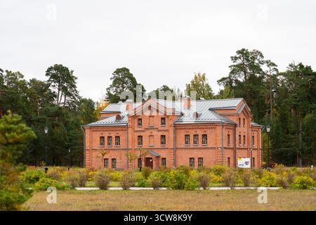 Ein herrliches, historisches, zweistöckiges Gebäude aus rotem Backstein, eingebettet in eine Lichtung und umgeben von einem dichten grünen Kiefernwald unter einem bewölkten Himmel Stockfoto