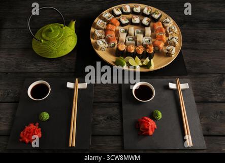 Sushi und Brötchen mit Teekanne auf schwarzem rustikalem Holz, Blick von oben Stockfoto
