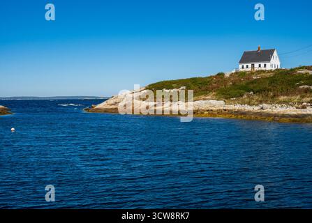 Peggy's Cove, NS - CA - 29. September 2025 Ein weißes Küstenhaus steht auf der felsigen Küste und dem blauen Wasser unter einem hellen, klaren Himmel in Nova Scotia. Stockfoto