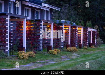 Karelien, Russland - 13. Mai 2024: Eine Nahaufnahme der gemütlichen, privaten Terrassen für moderne Apartments, beleuchtet in der Abenddämmerung und dekoriert mit einem schönen roten Klettergarten Stockfoto
