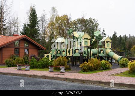 Otrakkala, Republik Karelien, Russland - 13. Mai 2024: Ein Holzgebäude mit rotem Dach steht neben einem großen, thematisch gestalteten Kinderspielplatz Stockfoto