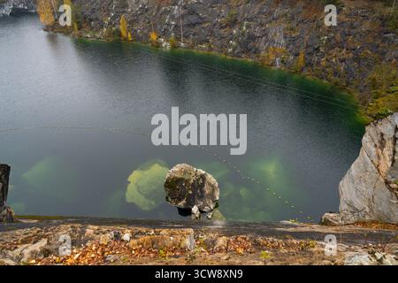 Hochwinkelaufnahme mit Blick in einen dunklen Steinbruchsee mit einem großen, einsamen Felsen oder einer Insel im Zentrum, umgeben von steilen Klippen Stockfoto