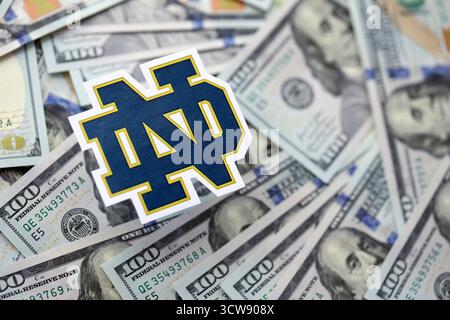 KIEW, UKRAINE - 23. FEBRUAR 2025 Notre Dame Fighting Irish Basketball Team Badge liegt auf einer großen Menge von hundert US-Dollar-Scheine Stockfoto