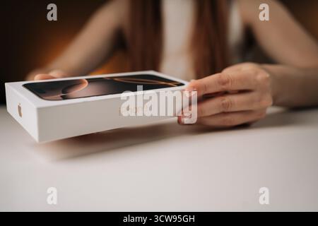 Nahaufnahme von jungen Frauenhänden, die das neueste iPhone 16 Pro auspacken und das moderne Smartphone-Design auf weißem Tisch enthüllen. Stockfoto