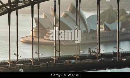 Australien, Sydney City: Das Sydney Opera House mit der Sydney Harbour Bridge bei Sonnenaufgang. Züge und Autos fahren auf der Straße, wobei die moderne Architektur und der städtische Verkehr in Australien hervorgehoben werden Stockfoto