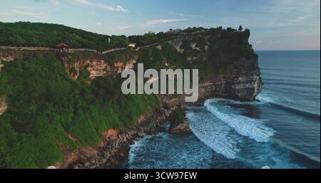 Luftdrohne fängt die atemberaubende Landschaft des Pantai Dreamland Beach in Bali, Indonesien, ein, mit Wellen, die gegen dramatische Klippen und üppige grüne Vegetation über die Landschaft stürzen Stockfoto