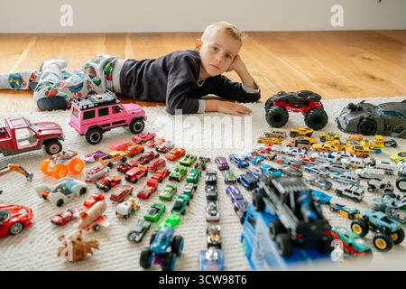 Blick von oben auf einen Jungen, der auf dem Boden liegt, umgeben von einer riesigen, farbenfrohen Sammlung von Spielzeugautos, die in Reihen angeordnet sind, Hobby- und Spielmöglichkeiten aus der Kindheit Stockfoto