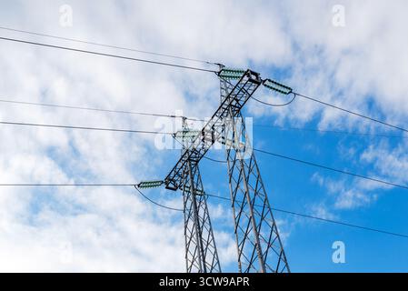 Stahlturm mit Hochspannungskabeln unter teilweise bewölktem blauem Himmel Stockfoto