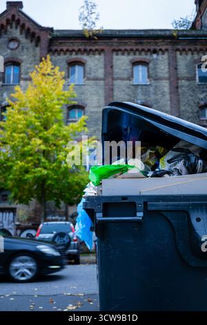Überlaufender Mülltonne vor einem historischen verlassenen Gebäude in Berlin, Deutschland, der auf städtische Abfälle und Verfall aufmerksam macht. Stockfoto