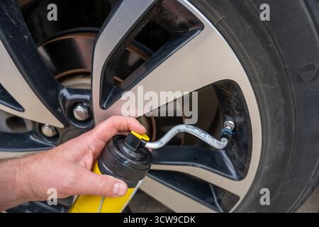 Selektiver Fokus auf chemisches Additiv, das aus einer Dose in einen Reifen gespritzt wird, um eine Panne zu reparieren Stockfoto