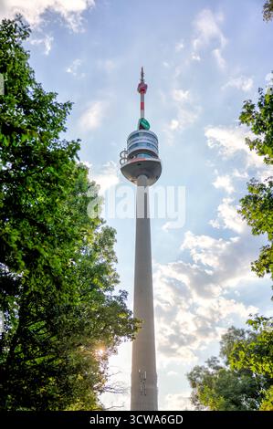 Der Donauturm erhebt sich über Bäumen im Donaupark unter hellem Sommerhimmel. Stockfoto