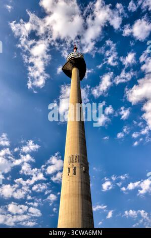 Der Donauturm erhebt sich über Bäumen im Donaupark unter hellem Sommerhimmel. Stockfoto