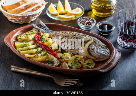 Appetitlicher gebackener dorado-Fisch mit Kartoffeln, Zitrone, rotem Chili und Gewürzen auf einer Tonplatte, Nahaufnahme. Gesundes Lebensmittelkonzept, gerösteter dorado mit Garn Stockfoto