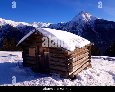 Eine charmante hölzerne Almhütte umgeben von tiefem Schnee in den Schweizer Alpen an einem hellen, sonnigen Wintertag im Engadin, Schweiz Stockfoto