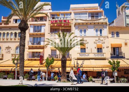 Sitges, Spanien - 1. Mai 2025: Blick auf Restaurants, Häuser und Menschen, die im Sommer auf der Promenade in Sitges, Katalonien, Spanien spazieren gehen Stockfoto