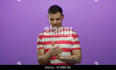 Junger hispanischer Mann in einem rot gestreiften Hemd steht vor einem isolierten lila Hintergrund mit einem durchdachten Ausdruck und ausdrucksstarken Handgesten. Stockfoto