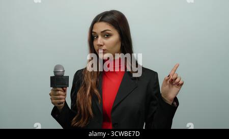 Die hispanische Reporterin hält ein Mikrofon, die mit einem Finger auf einem isolierten weißen Hintergrund ein Nein mit rotem Oberteil und schwarzer Jacke zeigt, was Kommunikation vermittelt Stockfoto