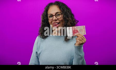 Frau mittleren Alters, die isländische Krone hält, lächelt vor leuchtendem lila Hintergrund. Stockfoto