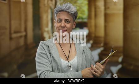 Frau mit kurzen grauen Haaren trägt einen grauen Hoodie und hält das gelbe Klemmbrett mit beiden Händen auf der Straße; Selbstvertrauen. Stockfoto