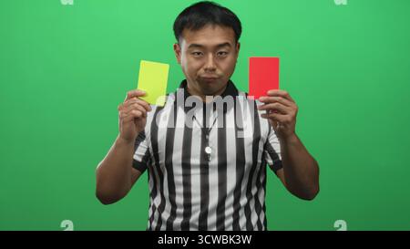 Der Schiedsrichter hält die rote und gelbe Karte und pfiff auf dem Schlüsselband in grünem Studio; Fairness. Stockfoto