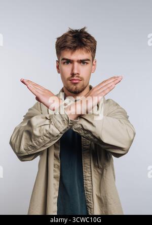 Porträt eines jungen Mannes, der seine Arme mit Autorität kreuzt, das Vertrauen symbolisiert und klare Grenzen auf weißem Hintergrund setzt Stockfoto