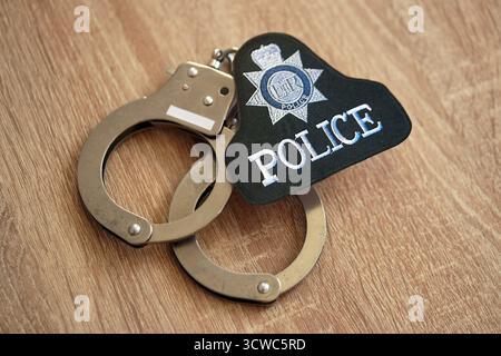 KIEW, UKRAINE - 17. SEPTEMBER 2025 Polizeiabzeichen des Vereinigten Königreichs mit Handschellen auf Holztisch Nahaufnahme Stockfoto