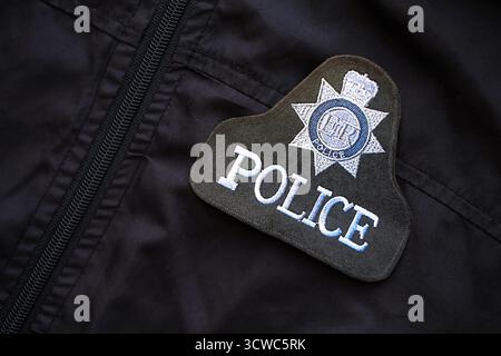 KIEW, UKRAINE - 17. SEPTEMBER 2025 Polizeiabzeichen des Vereinigten Königreichs auf schwarzer, einheitlicher Stoffoberfläche Nahaufnahme Stockfoto